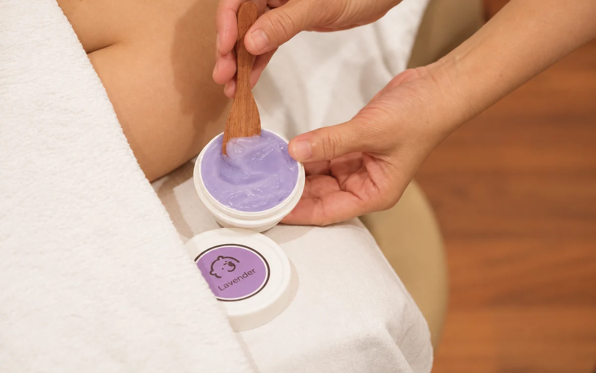 A close view of a purple balm bowl and a therapist’s hand