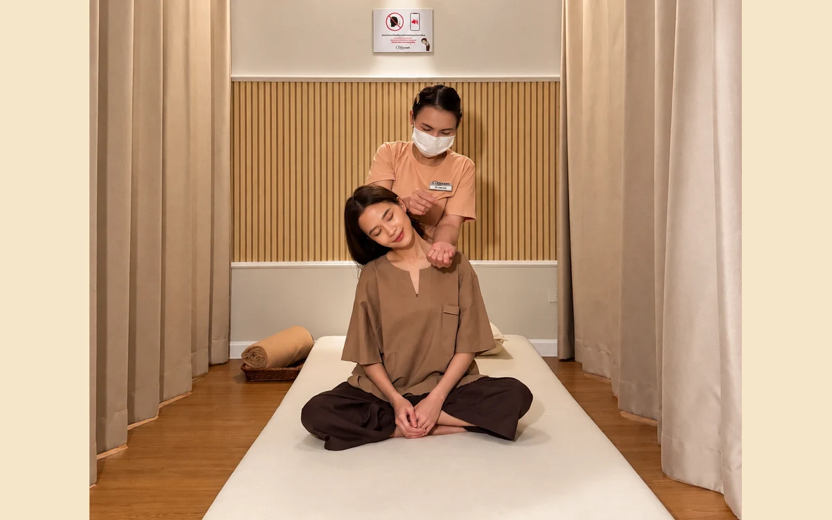 A therapist providing Thai massage from behind a seated guest